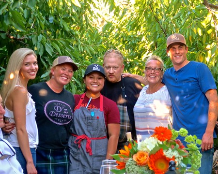 Group of people smiling in a vineyard, celebrating with flowers and wine, representing Lodi Winegrape Commission activities.