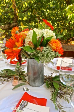 Colorful floral centerpiece with orange, white, and green flowers on a dining table for Lodi Winegrape Commission event.