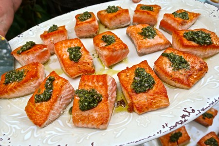Fresh salmon bites topped with green herb sauce on a decorative white platter.