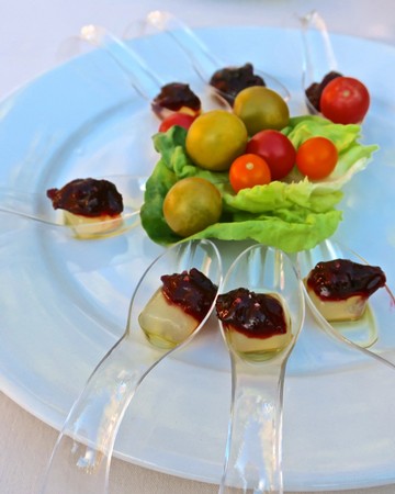 Elegant appetizer platter with grapes, cherry tomatoes, and cheese topped with jam, served on a blue plate.
