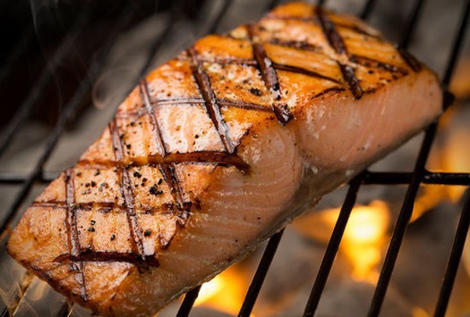 Fresh grilled salmon with grill marks cooking on a barbecue grill.