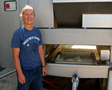 Woman in blue T-shirt standing next to wine grape processing equipment at Lodi Winegrape Commission.