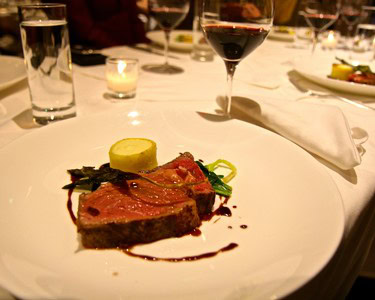 Elegant dinner plate with steak, lemon slice, and red wine glass at a fine dining restaurant.