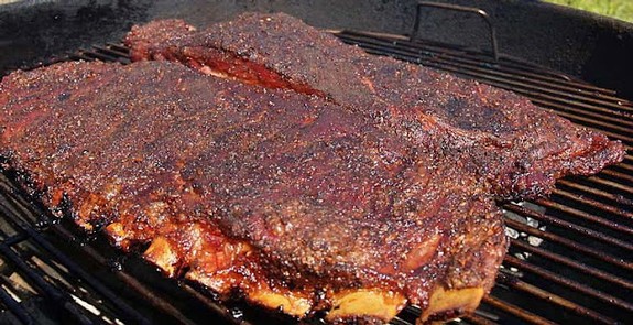 Juicy barbecue ribs with a smoky crust cooking on a grill.
