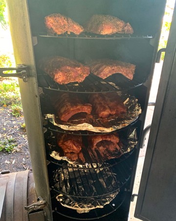 Barbecue ribs cooking in a smoker, showcasing the Lodi Winegrape Commission's focus on local wine and food pairing.