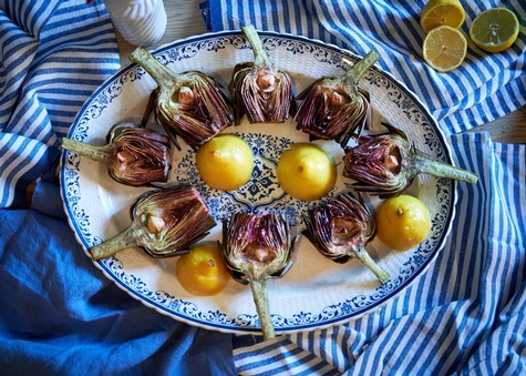 Fresh artichokes and lemons arranged on a decorative plate for culinary use.