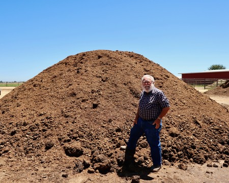 Man standing next to a large soil mound at a vineyard in Lodi, California, during daytime.