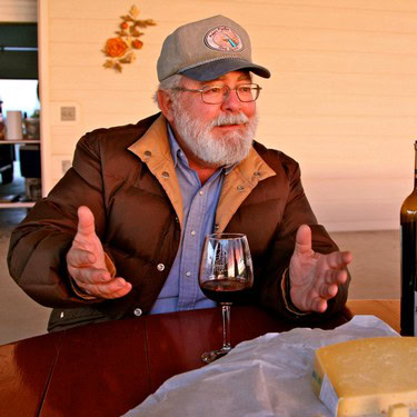 Elderly man with glasses and beard tasting wine at Lodi Winegrape Commission event.