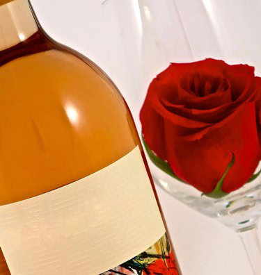 Bottle of wine and a red rose in a glass, representing Lodi Winegrape Commission's wine and vineyard culture.