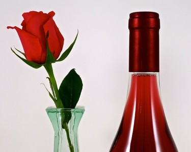 Close-up of a red wine bottle and a single red rose in a glass vase, representing Lodi Winegrape Commission.
