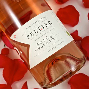 Lodi Winegrape Commission Rose of Pinot Noir in a glass with rose petals around it.