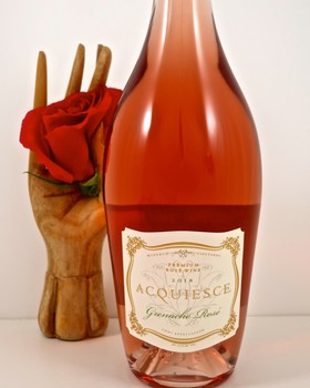Bottle of Acquese Grenache Rosé wine with a red rose and wooden fork in the background.