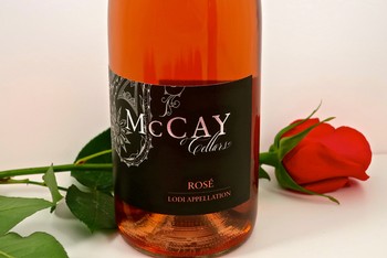 Bottle of McCay Cellars Rosé wine with a red rose flower beside it, on a white background.