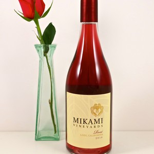 Mikami Vineyards rosé wine bottle with a single red rose in a glass vase.