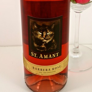 St. Amant Barbera Rosé wine bottle with a black cat label, on a white surface with a wine glass in the background.
