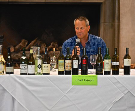 Chad Joseph speaking at wine tasting panel with various wine bottles on table.