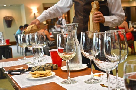 Wine glasses and a server pouring wine at a tasting event, with people in the background.