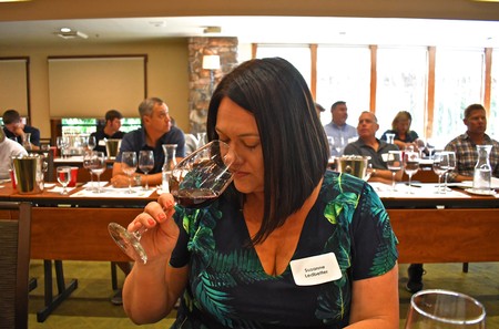 Woman tasting red wine at Lodi Winegrape Commission event with attendees in background.