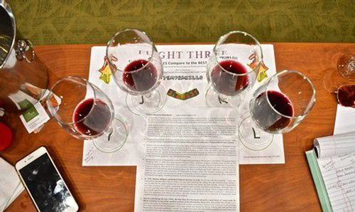 Four glasses of red wine on a table with tasting notes and a smartphone, representing Lodi Winegrape Commission activities.