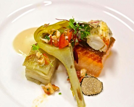 Elegant fish fillet with vegetables and herbs on a white plate, garnished with microgreens.