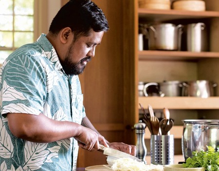 Chef preparing food in a cozy kitchen with wooden shelves and cooking utensils.