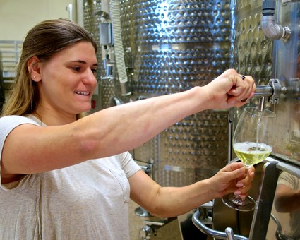 Woman pouring wine from a stainless steel tank during wine production at Lodi Winegrape Commission.