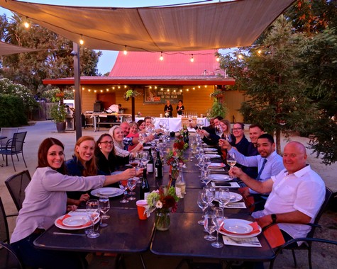 Group of people enjoying a dinner outdoors at a Lodi Winegrape Commission event with wine and food under string lights.