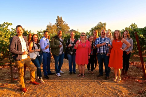 Group of diverse professionals at a vineyard in Lodi, California, during sunset, celebrating wine grape industry.