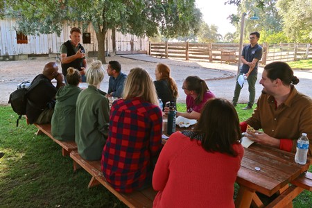 Group of people attending an outdoor educational event about Lodi winegrapes under trees.