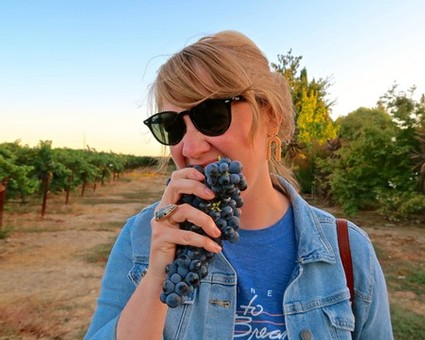 Woman with sunglasses tasting grapes in a vineyard during sunset.