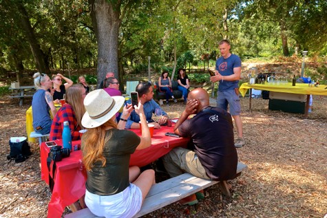 People gathered outdoors at a Lodi Winegrape Commission event, listening to a speaker in a park setting.