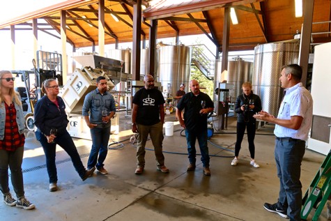 Group of people touring a winery with stainless steel tanks and a guide explaining the wine-making process.