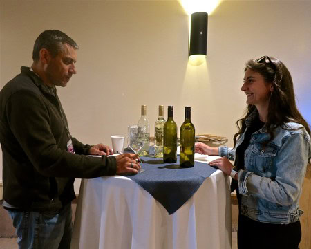 Two people enjoying a wine tasting at a Lodi Winegrape Commission event with bottles on a table.