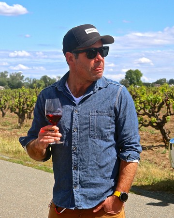 Man tasting red wine outdoors at Lodi vineyard, wearing sunglasses and casual denim shirt.