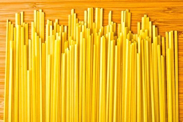 Uncooked yellow spaghetti pasta arranged on a wooden surface, ready for cooking or serving.