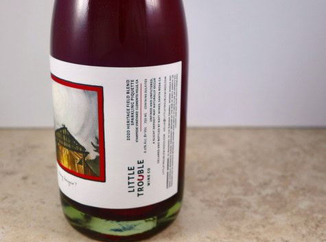 Close-up of Little Trouble wine bottle from Lodi Winegrape Commission, showing label details and deep red color.