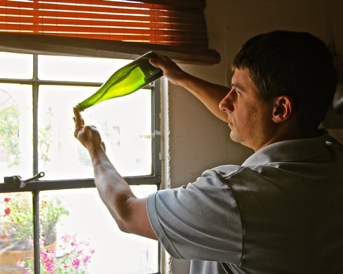 Man inspecting wine bottle near window, representing Lodi Winegrape Commission.