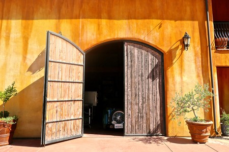 Entrance of a winery with large wooden doors, potted plants, and warm orange walls, representing Lodi wine region.