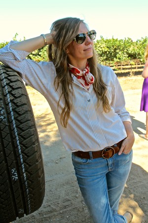 Woman in sunglasses leaning on a tire at a vineyard in Lodi, California, enjoying the wine country scenery.