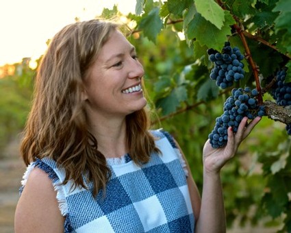Woman inspecting ripe grapes in a vineyard, showcasing Lodi winegrapes for wine production.