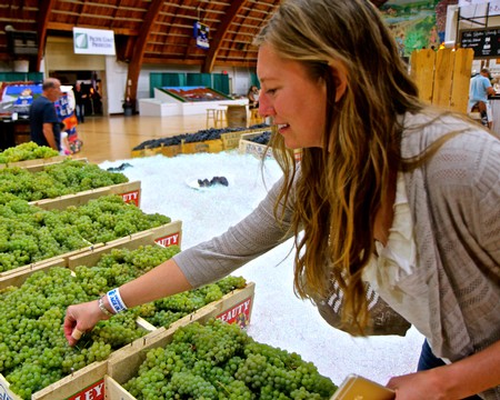 Woman selecting fresh green grapes at a market, promoting Lodi winegrapes and local agriculture.
