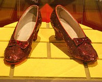 Pair of vintage red shoes with decorative bows on a yellow display stand.