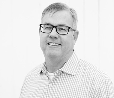 Portrait of a smiling man wearing glasses and a checkered shirt, professional headshot for Lodi Winegrape Commission.