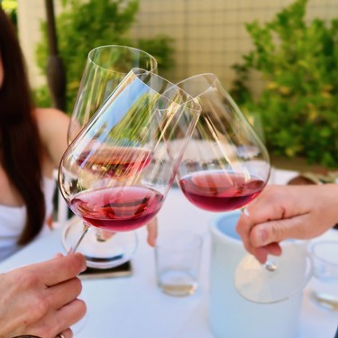 People clinking glasses of red wine outdoors, showcasing Lodi Winegrape Commission's wine quality and tasting experience.