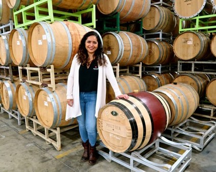Woman in winery with stacked wine barrels, promoting Lodi wine industry and winegrape production.