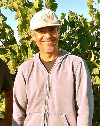 Smiling vineyard worker in Lodi wine region with grapevines in background.