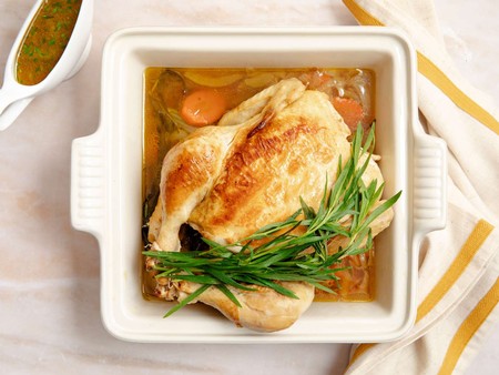 Baked chicken with carrots and green herbs in a white ceramic dish, served with gravy.