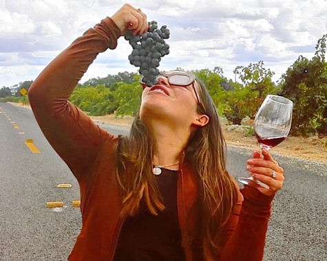 Woman tasting wine and holding a glass of red wine outdoors in a vineyard setting.
