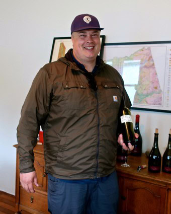 Smiling man holding a wine bottle at Lodi Winegrape Commission event with wine bottles and map in background.
