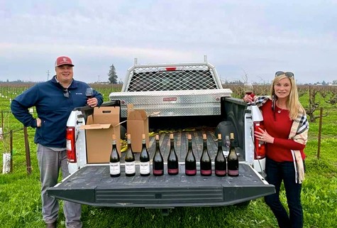 Two people with wine bottles and boxes in a vineyard during harvest at Lodi Winegrape Commission.